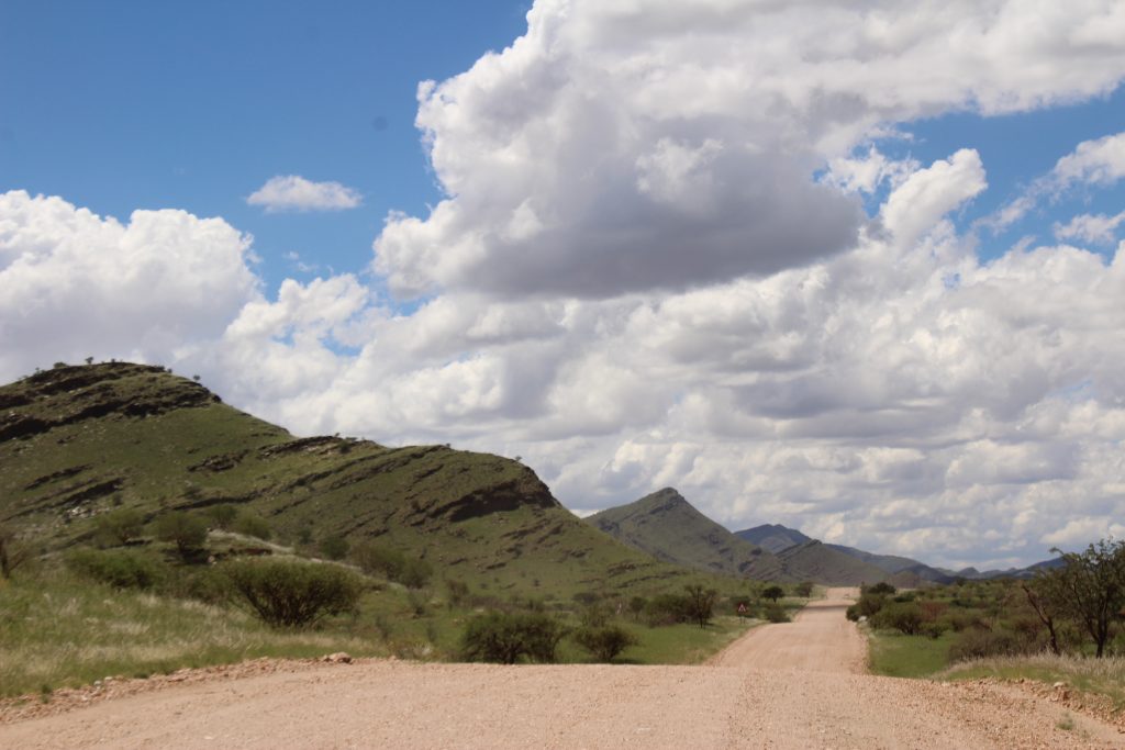 Gravel road through green hills and dramatic clouds during Namibia's green season