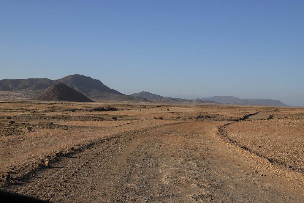 Vast desert plain with volcanic mountains on the horizon, viewed from a vehicle in Damaraland, Namibia